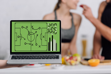 selective focus of laptop with football scheme on screen near couple in kitchen