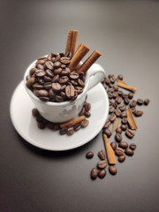 scattered coffee beans, a Cup with coffee beans and cinnamon sticks on a black background.