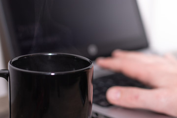 Fototapeta na wymiar Black coffee mug with coffee with laptop, hand working in the background