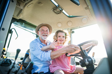 Senior farmer with small granddaughter sitting in tractor, driving.