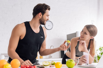 happy man with sliced apple near girl with smoothie and laptop