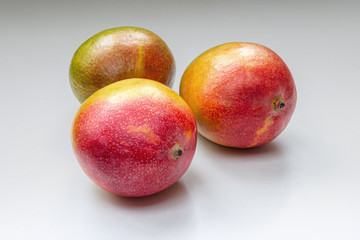 Ripe, juicy tropical mangoes on a light gray surface