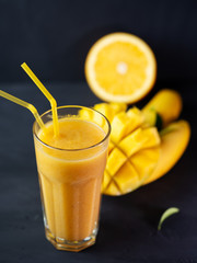 A glass of fresh yellow mango, banana and orange smoothie.