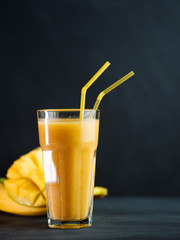 A glass of fresh yellow mango, banana and orange smoothie.