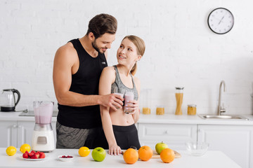 happy man and woman clinking glasses with smoothie near fruits