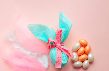 Egg gift in green paper packaging and with pink ribbon Easter Bunny wrap idea. Chocolate dragee white and gold color, multicolor colorful feathers. Minimal concept. Flat lay, Copy space, top view