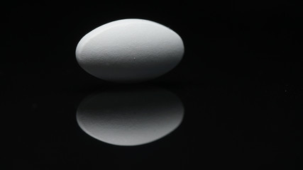 white oval tablet isolated on a black background with reflections. the concept of drugs.