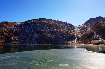 Under the nice blue sky covered with thin ice the Tsomgo Lake or Changu Lake water surrounded by...