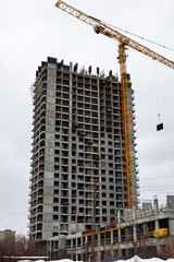 building at a construction site made of reinforced concrete frame with a crane against a gray sky