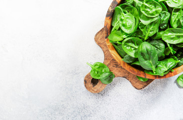 Fresh baby spinach leaves in wooden bowl on gray stone table. Top view, copy space
