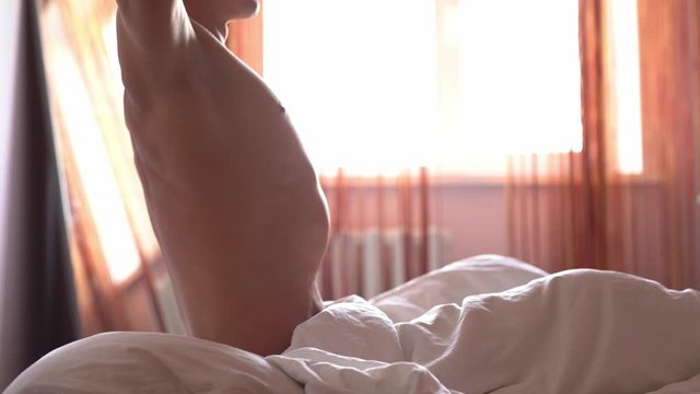 Handsome young man Sleeping Cozily in Bed, waking up in the Morning and lazily stretching. Young and Fit Caucasian Man Greeting New Day.