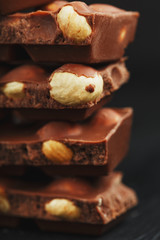 Chocolate with hazelnut in the form of a tower on a dark background. Pieces of milk chocolate with nuts.