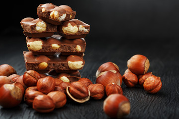 Chocolate with hazelnuts in the form of a tower on a dark background, surrounded by nuts in the shell and peeled.