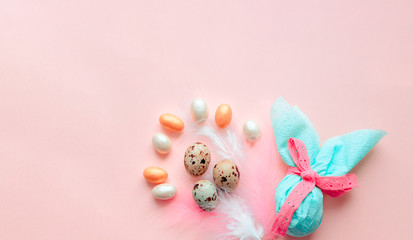 Fototapeta na wymiar Egg gift in green paper packaging and with pink ribbon Easter Bunny wrap idea. Chocolate dragee white and gold color, multicolor colorful feathers. Minimal concept. Flat lay, Copy space, top view