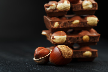 Chocolate with hazelnuts in the form of a tower on a dark background, surrounded by nuts in the shell and peeled.