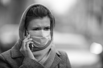 Young woman in a protective mask talking on a smartphone on the street