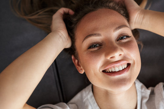 Image of happy caucasian woman smiling at camera while lying on couch