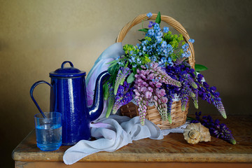 Still life with lupine flowers in a basket and a blue kettle on a table on a brown background