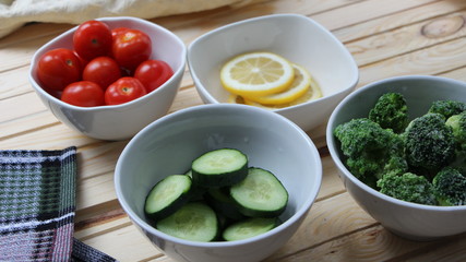 vegetables and lemon slices in white bowls on a light wooden table