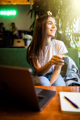 Beautiful woman dreaming about something while sitting with laptop in modern cafe bar