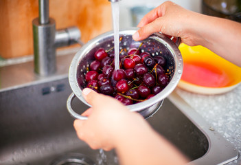 Woman hands washing cherries in colander in kitchen sink.