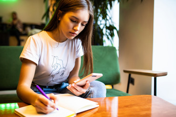Young woman writes in her planner and holds mobile phone working freelance place