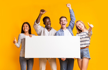 Joyful teenagers with empty billboard showing thumbs up