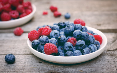 Still life with a blueberries and raspberries on an old wooden table, at the garden. Rural natural food style.