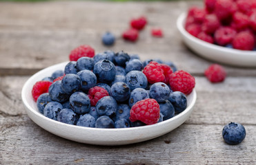 Still life with a blueberries and raspberries on an old wooden table, at the garden. Rural natural food style.