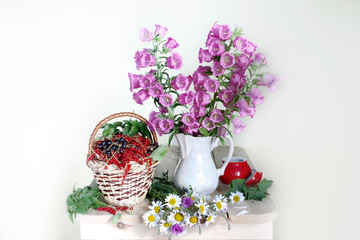 Still life with bells and daisies in a vase and berries on a light background.Summer bouquet on the table.