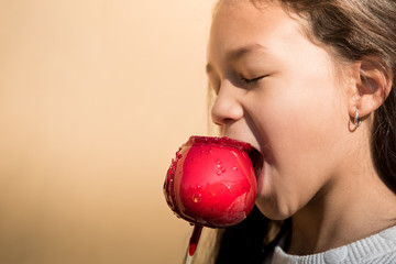 Beautiful latin girl biting a red caramel apple on a isolate orange background