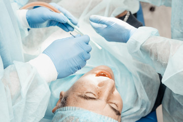 Dentists will perform an operation, implant placement. Real operation. Tooth extraction, implants. Professional uniform and equipment of a dentist. Healthcare Equipping a doctor’s workplace. Dentistry