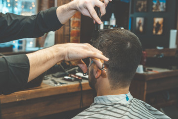 Haircut at the hairdresser. Barber cuts the hair on the client's head. The process of creating hairstyles for men. A man in a barbershop. The near plan. Equipment stylist. Selective focus