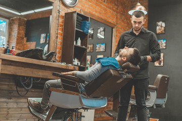 Beauty shop for men. Shaving a beard in a barbershop. Barber cuts his beard with a razor and clipper. close up Brutal haircuts. Hairdresser equipment. Selective focus.