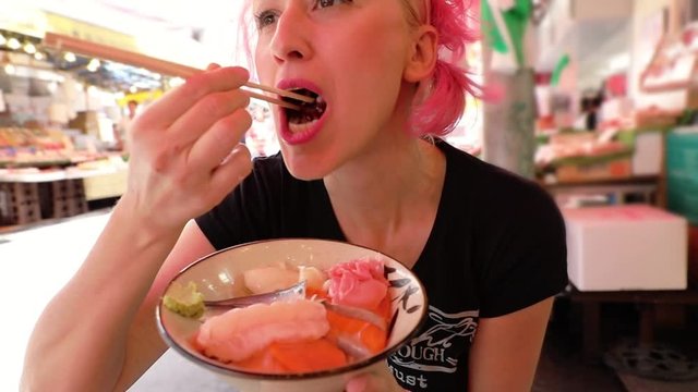 SLOW MOTION: Caucasian tourist woman eats with chopsticks, sashimi salad at Ameya-Yokocho market street near Ueno in Tokyo, Japan. Ameyoko is a very popular attraction for Japanese lifestyle tourism