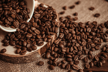 A Cup of coffee with scattered coffee beans on a burlap on a wooden background. Roasted natural coffee