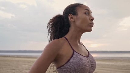 A serious young african american woman in sportswear is doing exercises on her shoulders on the beach in the morning