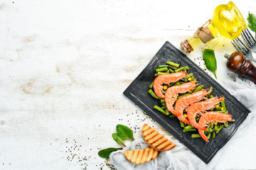 Boiled shrimps and green beans on a black stone plate. Rustic style. Top view. Free space for your text.
