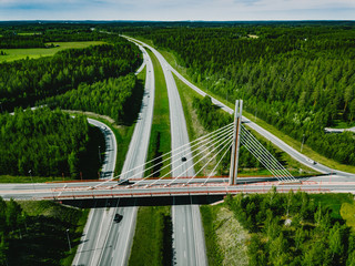 Aerial top view of cable-stayed Suspension bridge and Highway road with green forests in Finland.