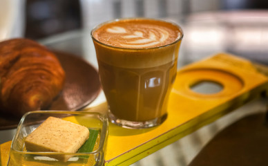 Cappuccino in a glass cup and a small cracker on a banana leaf