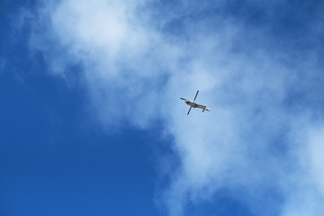 A seaside nautical search and rescue helicopter with rotating blades in the distance with a vivid bright blue sky and clouds. Rescue helicopter and rescue teams are brave.