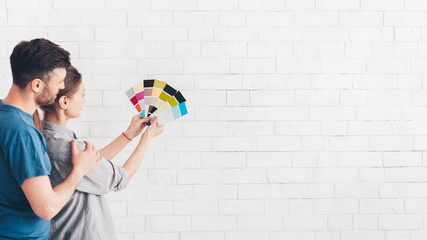 Embracing couple looking at color samples at home