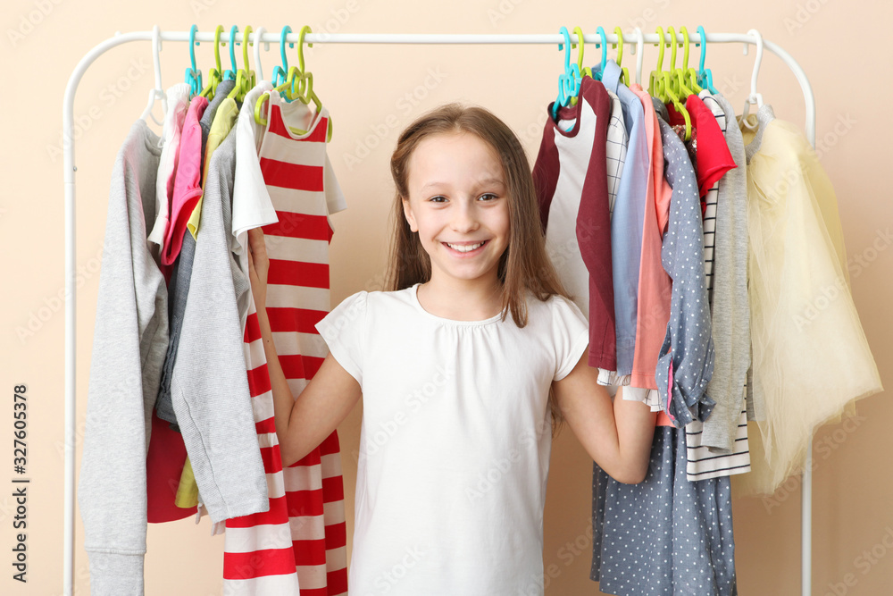 Wall mural cute cheerful little girl chooses clothes with floor hangers. children's clothing, children's shoppi