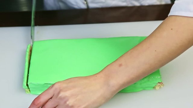 confectioner cut off by knife one of edges of rectangle green glazed layered cake