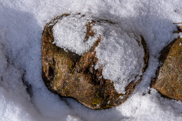 Landscaping: the design of flower beds in large stone against the background of thawed spring snow and spring sunshine.