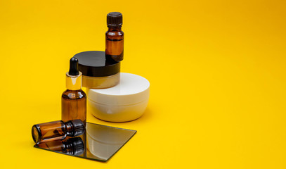 Set of cosmetic products with serum, face cream on a bright sandy yellow background with a mirror. Beauty blogger, procedures salon concept. Minimalism.