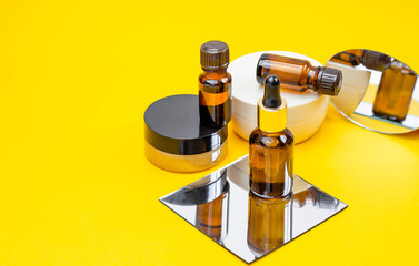 Set of cosmetic products with serum, face cream on a bright sandy yellow background with a mirror....