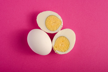 Obraz na płótnie Canvas Boiled egg with yellow yolk near to white eggs on vibrant purple pink plain minimal background, top view, happy Easter day, copy space
