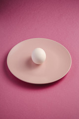White egg in pink plate on purple plain minimal background, angle view, happy Easter day