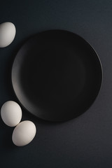 White eggs near to black plate on dark moody plain minimal background, top view, happy Easter day